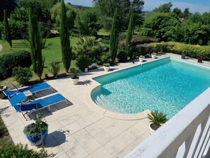 A rectangular swimming pool with a curved edge, surrounded by a tiled deck with lounge chairs and potted plants.