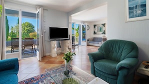 A living room with a TV, a green armchair, a sofa, and a dining area with a table and chairs.