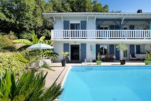A two-story house with a swimming pool, surrounded by lush greenery and a patio with outdoor furniture. - Ground-Floor Apartment for 2–3 Guests in Périgord Pourpre with Pool (Prigonrieux)