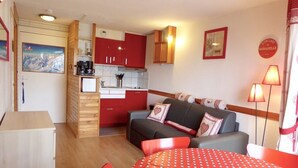 Un espacio habitable compacto con kitchenette, un sofá, una mesa de comedor y un cuadro en la pared.