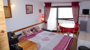 Una habitación con cama, escritorio, silla, mesa, televisor y balcón con mesa y sillas.