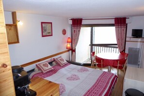 A room with a bed, a desk, a chair, a table, a TV, and a balcony with a table and chairs. - Vrbo Property (Saint-Lary-Soulan)
