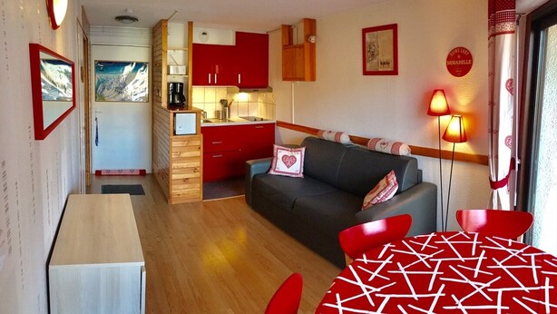 Una habitación compacta con kitchenette, un sofá, una mesa y una lámpara.