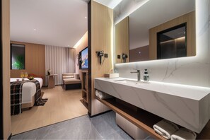 Et moderne hotelværelse med et stort badeværelsesbord-arrangement, en seng med udsigt og et opholdsområde med et fjernsyn.