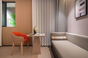 Et moderne hotelværelse med sofa, stol, lille bord og et vindue med gardiner.