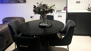 Ein runder Tisch mit Stühlen, eine Vase mit Blumen, ein kleiner Tisch mit einer Flasche und ein Sofa.