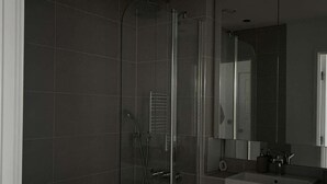 Ein modernes Badezimmer mit Duschkabine aus Glas, einem weißen Waschbecken und einem großen Spiegel.