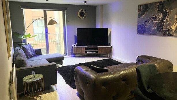 Ein modernes Wohnzimmer mit einer Couch, einem Ledersessel, einem Flachbildfernseher und einem Bild an der Wand.