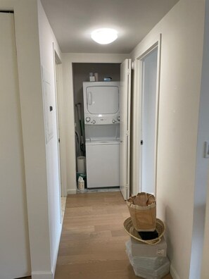 Een wasruimte met een wasmachine, een droger, een mand en een prullenbak.