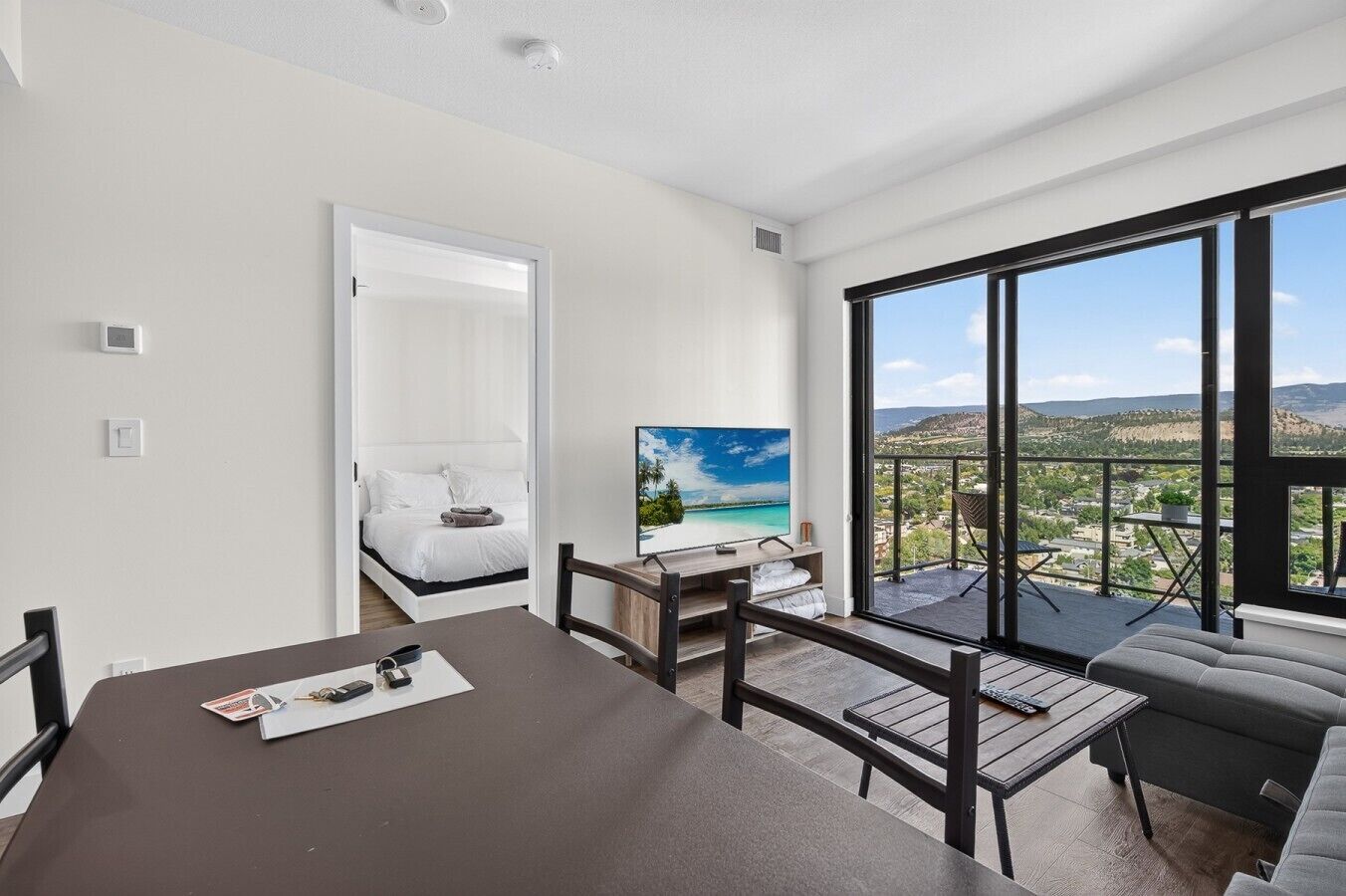 Ein modernes Hotelzimmer mit Balkon, einem Bett, einem Fernseher und einer Essecke.