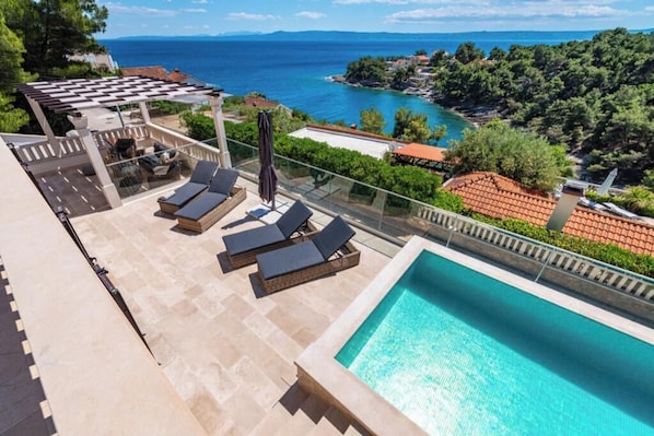 A rooftop pool with lounge chairs, a pergola, and a view of the sea and coastline. - Villa Kadena (Selca, Brač)