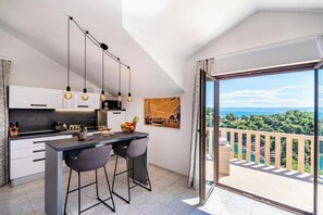 A modern kitchen with a bar area, a dining set, and a large balcony with a scenic view. - Villa Kadena (Selca, Brač)