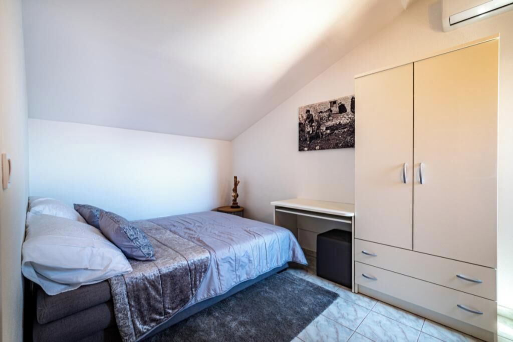 A bedroom with a bed, a desk, a wardrobe, and a wall-mounted picture.