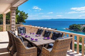 A dining area with a table set for four, wicker chairs, and a view of the sea. - Villa Kadena (Selca, Brač)