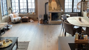 Een rustiek interieur met een open haard, houten vloeren en grote ramen.