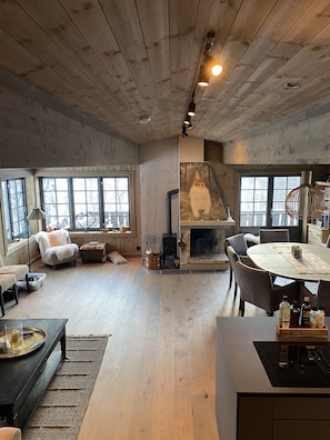 Ein rustikales Interieur mit Kamin, Holzdielen und großen Fenstern.