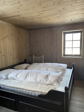 Una habitación con paneles de madera, una cama, una ventana y una rejilla de ventilación en el techo.