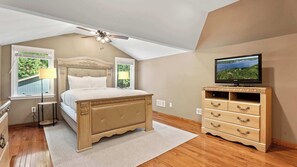 Ein Schlafzimmer mit einem Bett, einem Deckenventilator, einem Fernseher und einer Kommode.