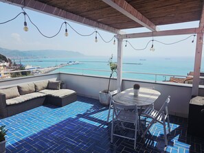 Un balcon avec vue sur la mer, un coin salon et une table avec des chaises.