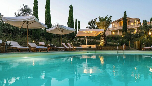 A swimming pool with lounge chairs and umbrellas, surrounded by tall trees and a building with balconies. - Historic villa with private pool near Florence (Vinci)