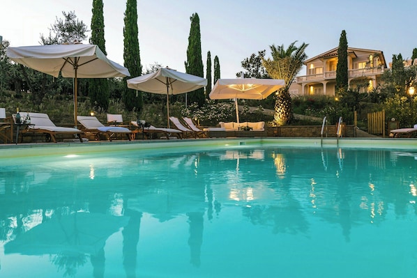 A swimming pool with lounge chairs and umbrellas, surrounded by tall trees and a building with balconies. - Historic villa with private pool near Florence (Vinci)