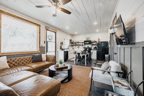 Una sala de estar moderna con un sofá de cuero, una mesa de comedor y una cocina con un refrigerador negro y armarios blancos.