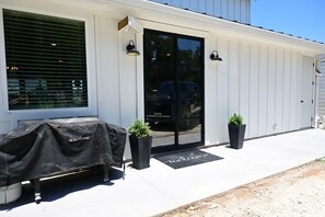 A building with a black door, a covered grill, and two potted plants on the sidewalk. - 3 Houses a Farm Sleeps 20, Swimming Hole, Pools, Hot Tubs, Views (Spring Branch)