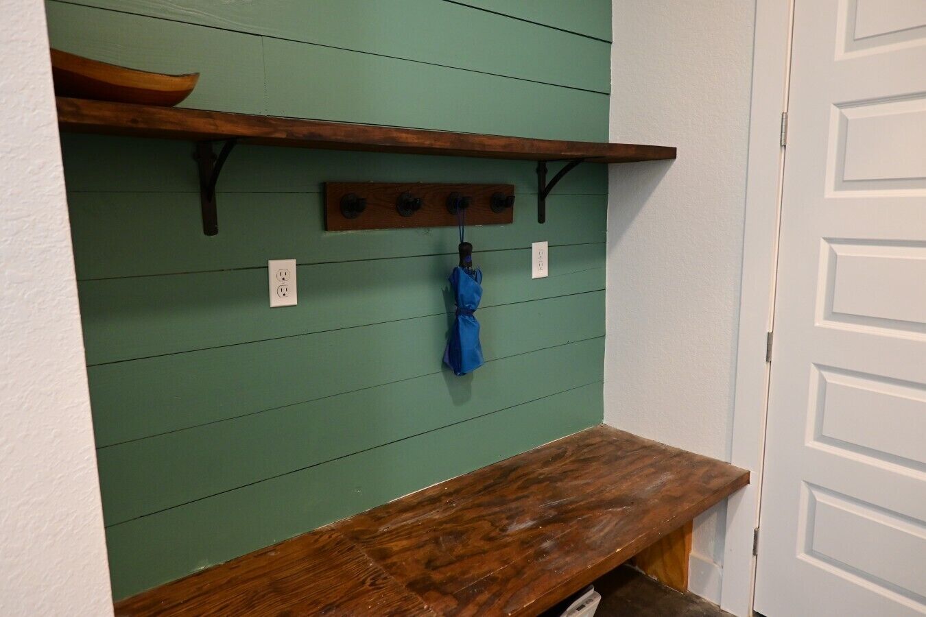 Una pared verde con un estante de madera, una toalla azul colgada y una puerta blanca.