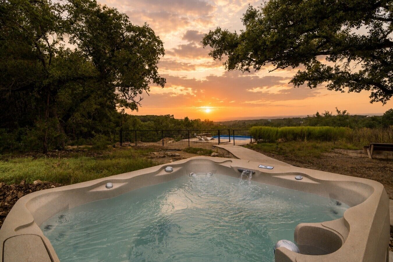 A hot tub with a view of the sunset, surrounded by trees and a fenced area.