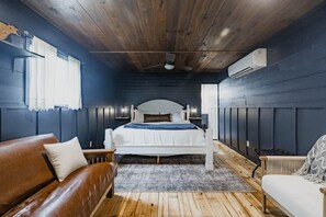 A bedroom with a wooden ceiling, a bed with white bedding, a brown leather sofa, and a white armchair. - 3 Houses a Farm Sleeps 20, Swimming Hole, Pools, Hot Tubs, Views (Spring Branch)