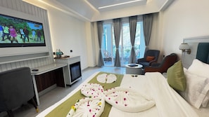 A hotel room with a bed, a TV, a desk, a chair, and a balcony with curtains. - Arista Haven Hotel (Narendranagar)