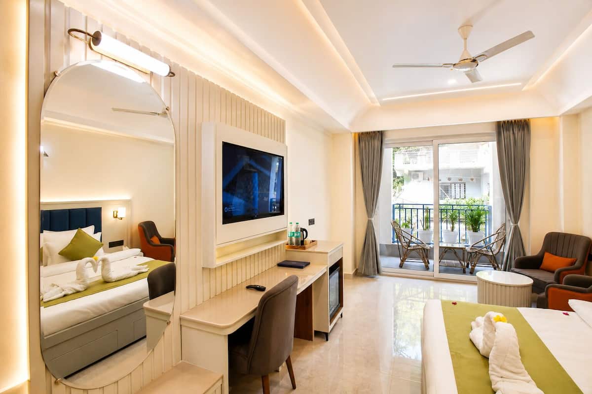 Habitación de hotel con cama, escritorio, televisor y balcón con sillas.