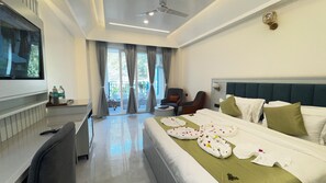 Habitación de hotel con cama, escritorio, silla, televisión y balcón con cortinas.