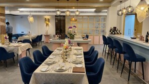 A restaurant with multiple dining tables, blue chairs, and hanging pendant lights. - Arista Haven Hotel (Narendranagar)