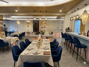 A restaurant with multiple dining tables, blue chairs, and hanging pendant lights. - Arista Haven Hotel (Narendranagar)