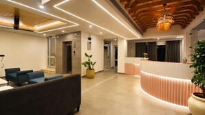 A modern hotel lobby with a reception desk, seating area, and a staircase leading to an upper level. - Arista Haven Hotel (Narendranagar)