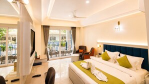 A hotel room with a balcony, a bed with pillows, a chair, a bedside table, and a TV. - Arista Haven Hotel (Narendranagar)
