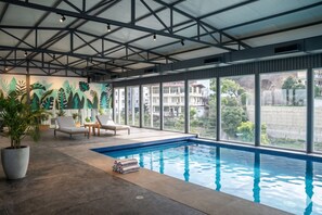 Una piscina con vistas a edificios, un techo con diseño de cuadrícula y una pared decorada con motivos de hojas.