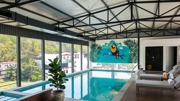 A modern indoor pool area with a large window, a mural of a bird, and lounge chairs. - Arista Haven Hotel (Narendranagar)