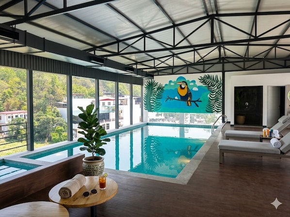 A modern indoor pool area with a large window, a mural of a bird, and lounge chairs. - Arista Haven Hotel (Narendranagar)