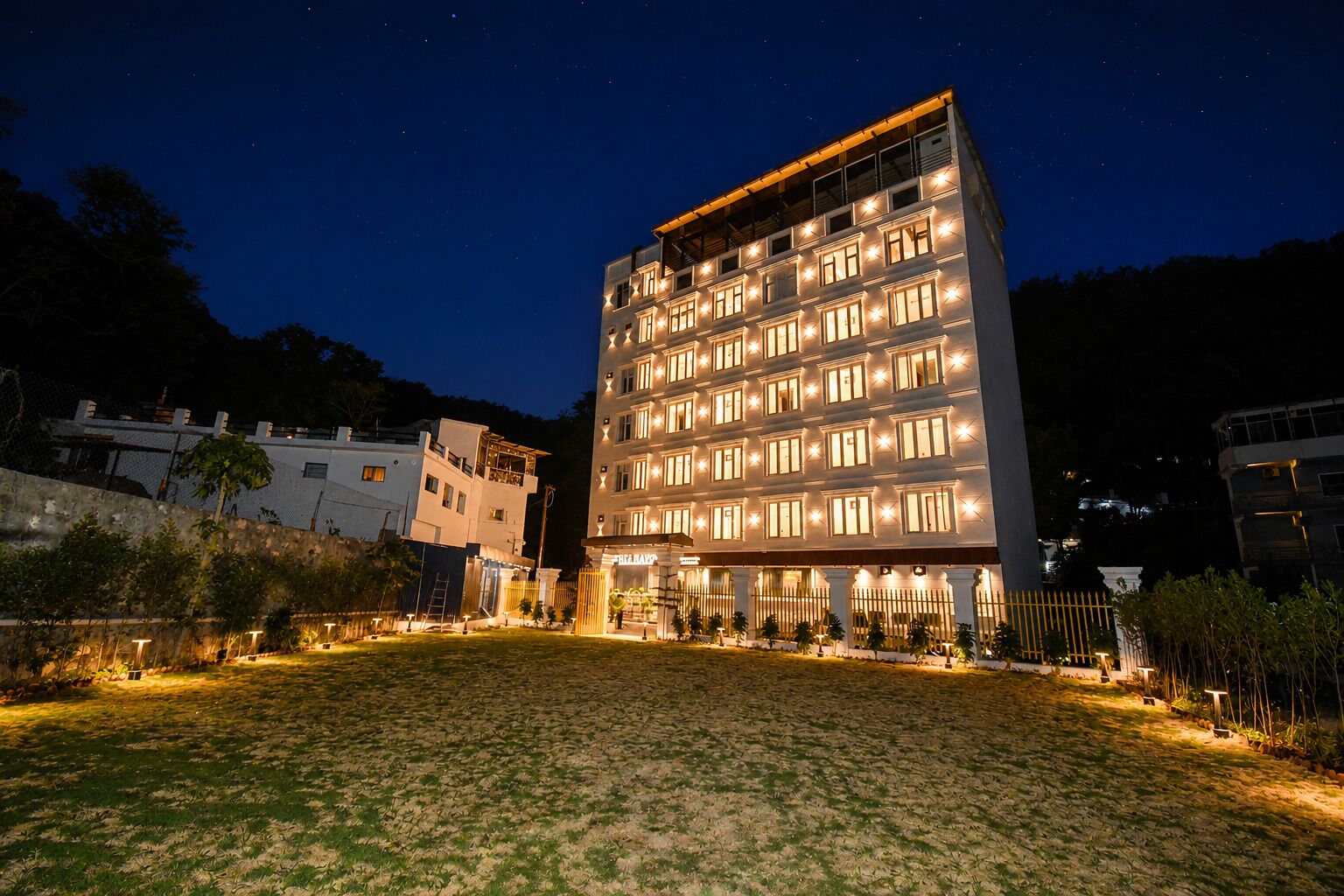 A multi-story hotel with illuminated windows, a well-lit courtyard, and a view of the surrounding area at night.