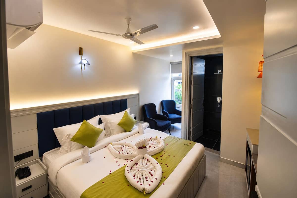 Una habitación de hotel con una cama, un ventilador de techo, una mesita de noche con un teléfono y una silla en la esquina.