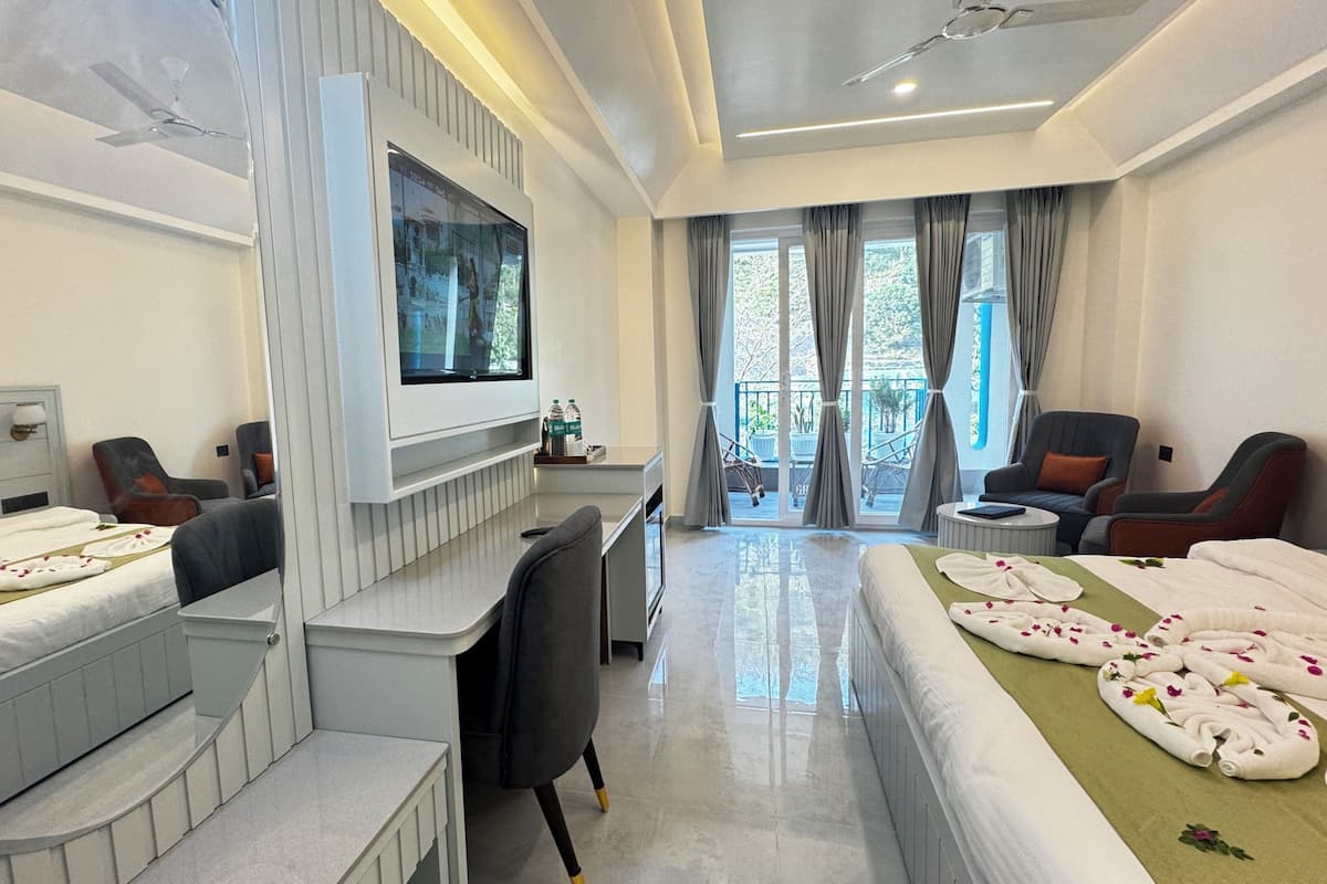 A hotel room with a bed, two chairs, a desk, a TV, and a balcony with curtains.