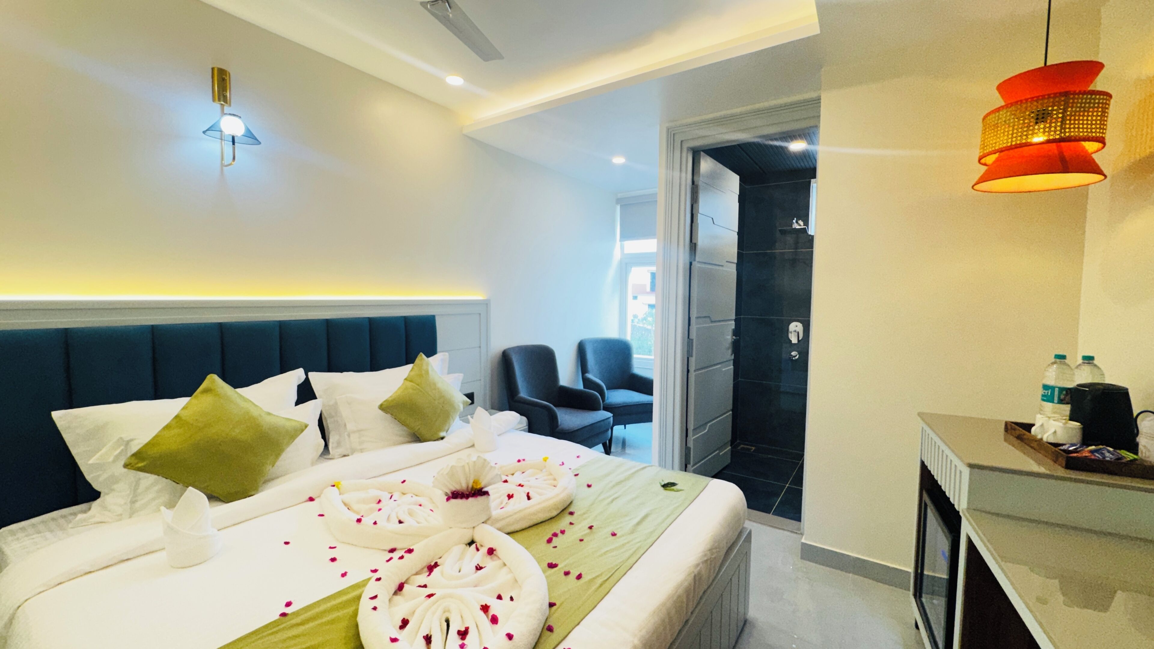 A modern hotel room with a neatly made bed, a seating area with chairs, and a desk with a water bottle.