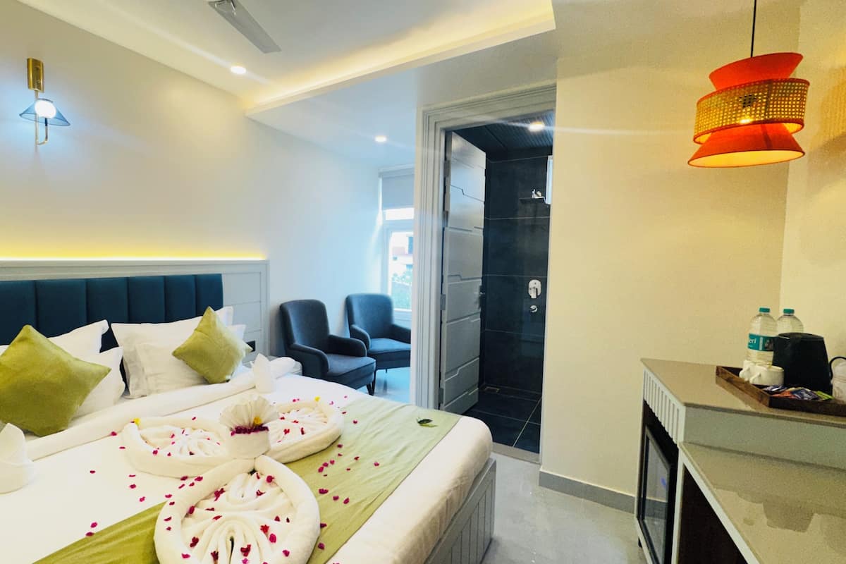 Une chambre d’hôtel moderne avec un lit bien fait, un coin salon avec des fauteuils et un bureau avec une bouteille d’eau.