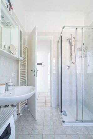 Ein modernes Badezimmer mit einer Duschkabine aus Glas, einem weißen Waschbecken und einem Spiegel darüber.