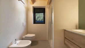 Et lille badeværelse med toilet, bidet og et vindue.