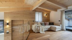 Ein modernes Interieur mit Holzwänden, einer Couch, einem Fenster mit Vorhängen und Blick auf eine verschneite Landschaft.