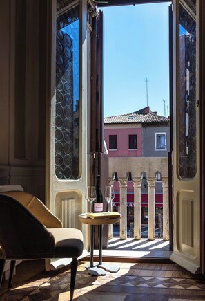 An open door with a view of buildings, a table with a bottle and glass, and a chair inside. - Attilia Suite Historical House in Chioggia canal view Vena Laguna di Venezia (Chioggia)
