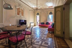 A dining area with a round table and chairs, a television, and a sofa with cushions. - Attilia Suite Historical House in Chioggia canal view Vena Laguna di Venezia (Chioggia)